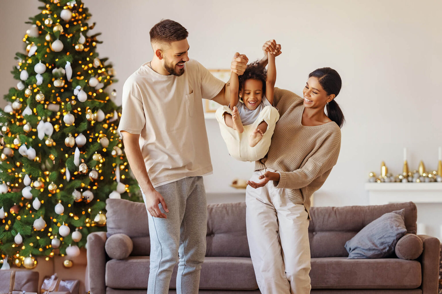 full-body-multiethnic-father-mother-smiling-lifting-mixed-race-son-near-couch-cozy-living-room2