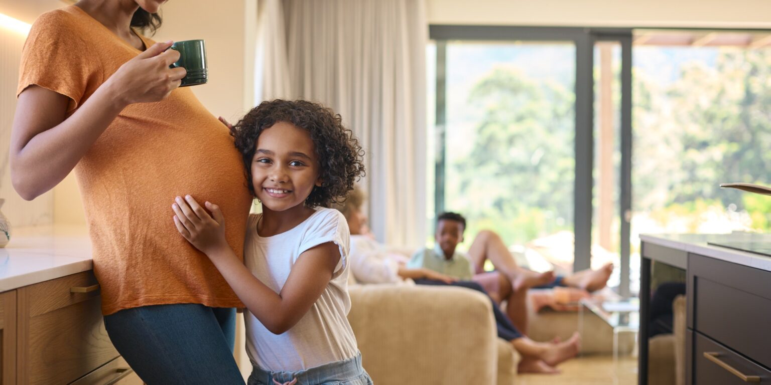 Multi Generation Family At Home As Daughter Listens To Baby's Heartbeat In Pregnant Mother's Tummy